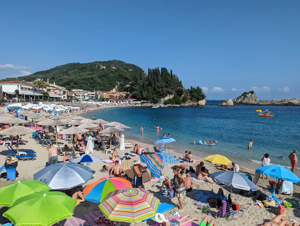 Beach day in Greece, beautiful blue sea with many people sun bathing or in the water, with some rocks in the background