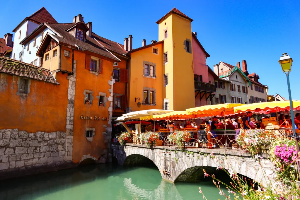A view of a French city, photo shot over a river showing a bridge full with people entering the old city