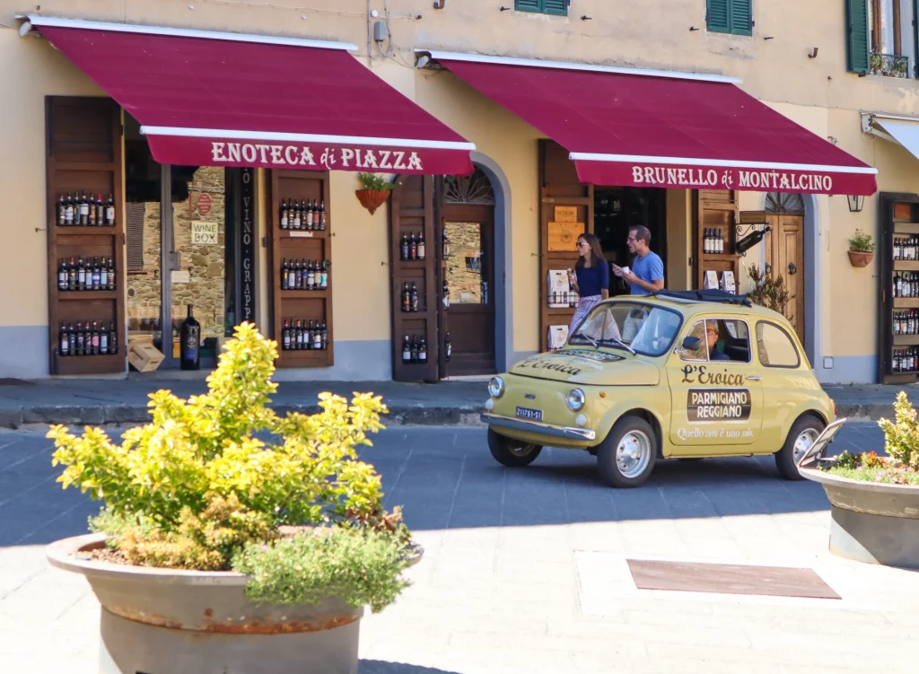 A yellow classic car passing by in front of a vine shop in Italy