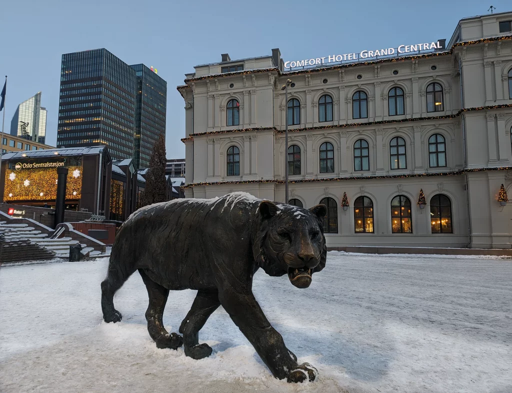 View from the side of Oslo central bus station with an iconic lion statue in foreground during Christmas period with a Hotel in the background.