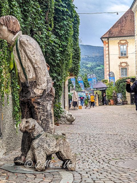 Paved street, a wood sculpture of a man and dog, with a boy riding on one wheel a mountain bike.