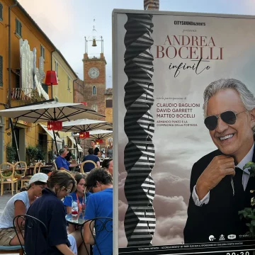 A market with people and a big poster of Andrea Bocelli advertising a concert