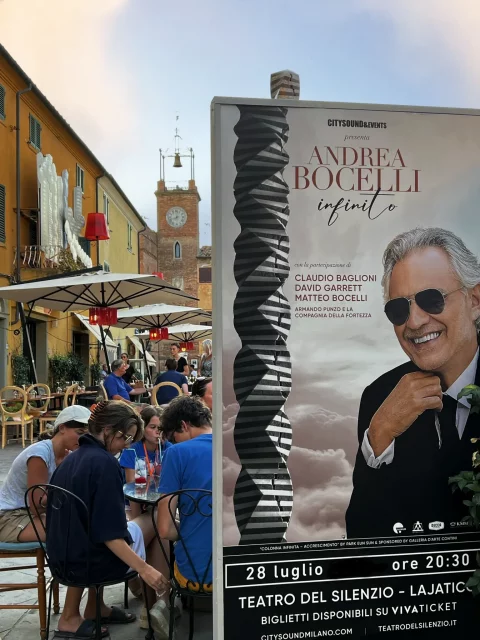A market with people and a big poster of Andrea Bocelli advertising a concert