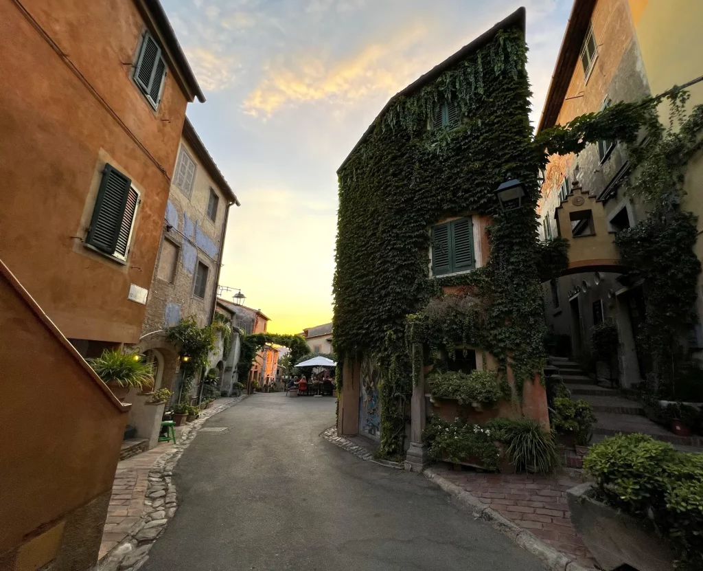 A street at sunset, surrounded with old houses full with hanging greenery on the walls, beautiful yellow-orange sunset