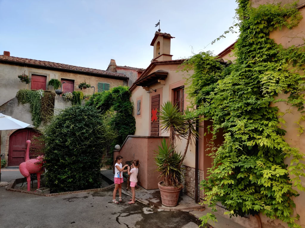 A small street, with children playing in a near a old house , and a massive turkey statue, coloured pink in one side