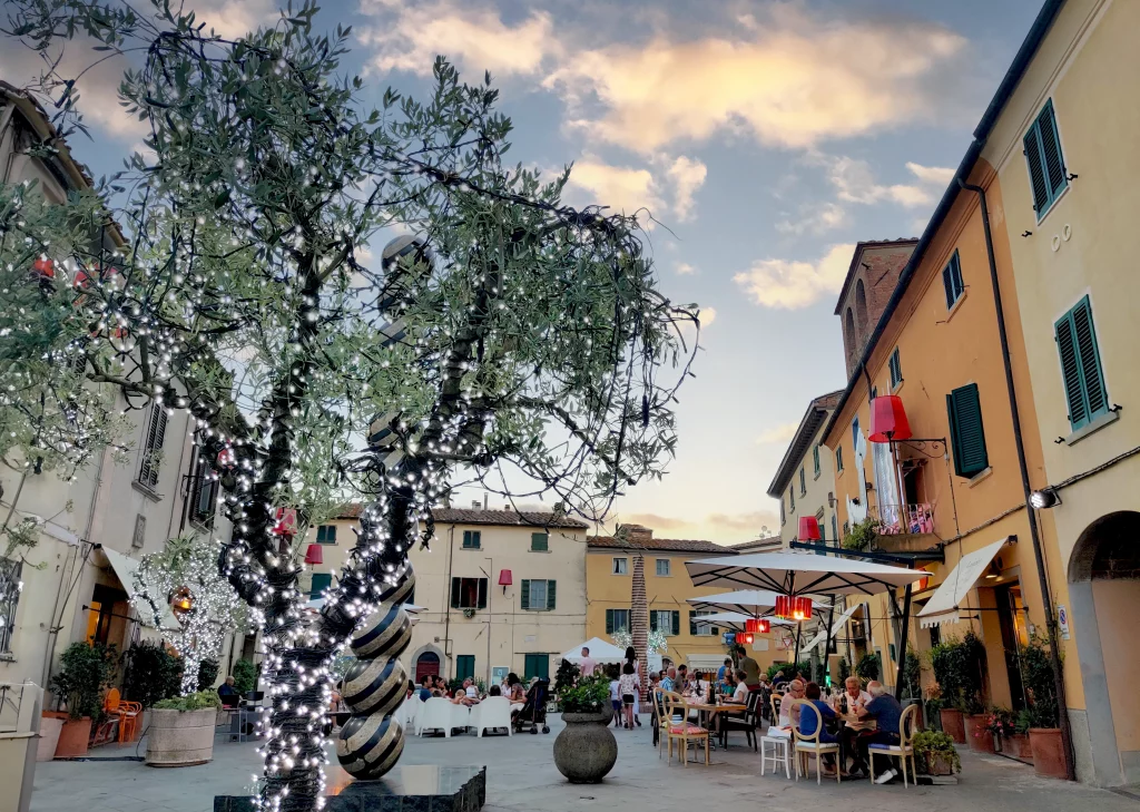 a communal square with restaurants and people sitting at tables around the area