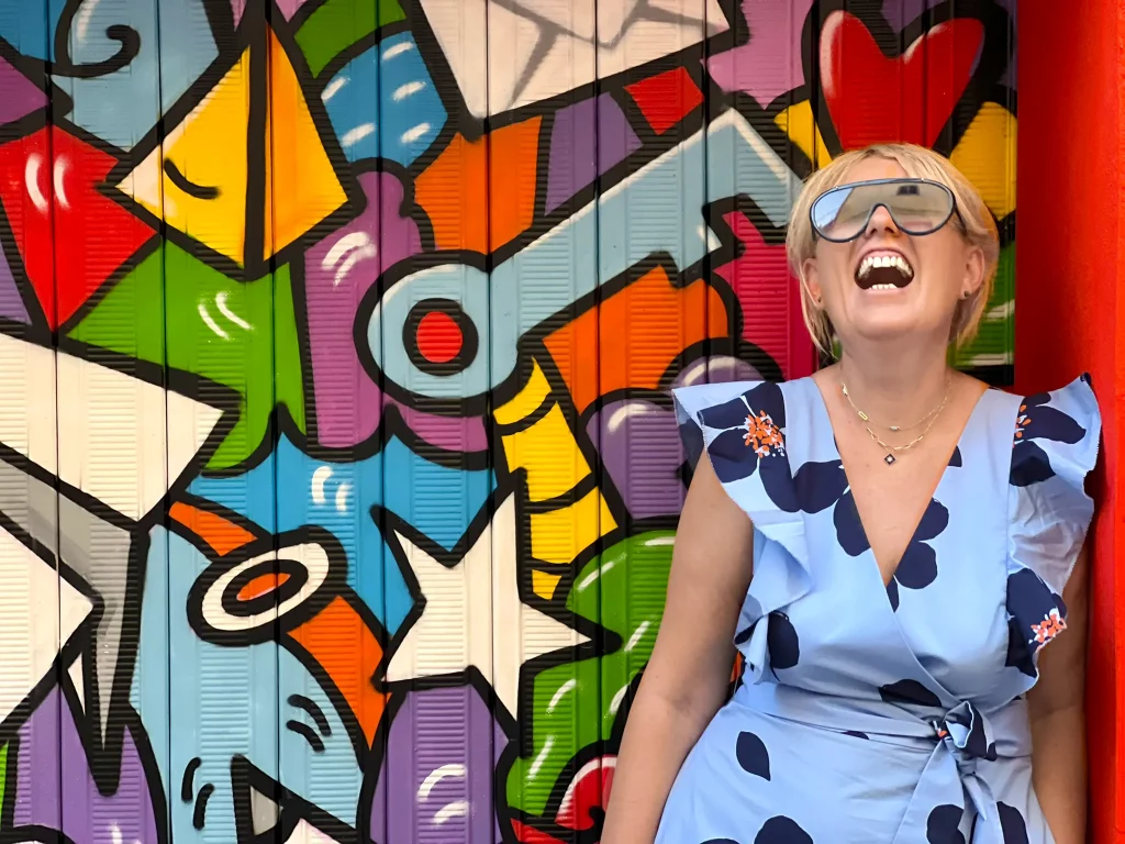 a woman laughing in front of a piece of abstract street art painted on a garage door