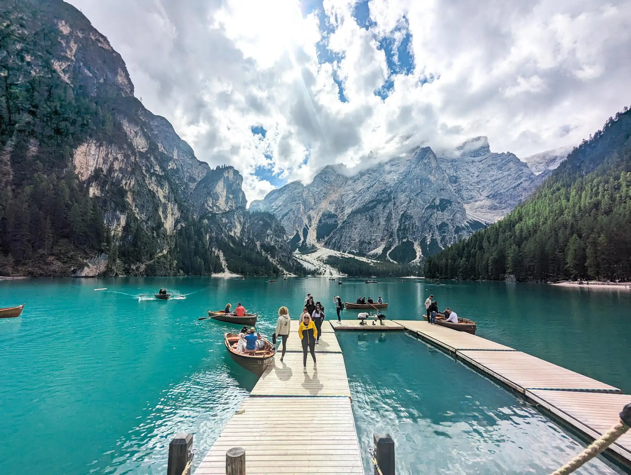 People on a floating pontoon floating on a blue lake, rowing boats with mountains in the background