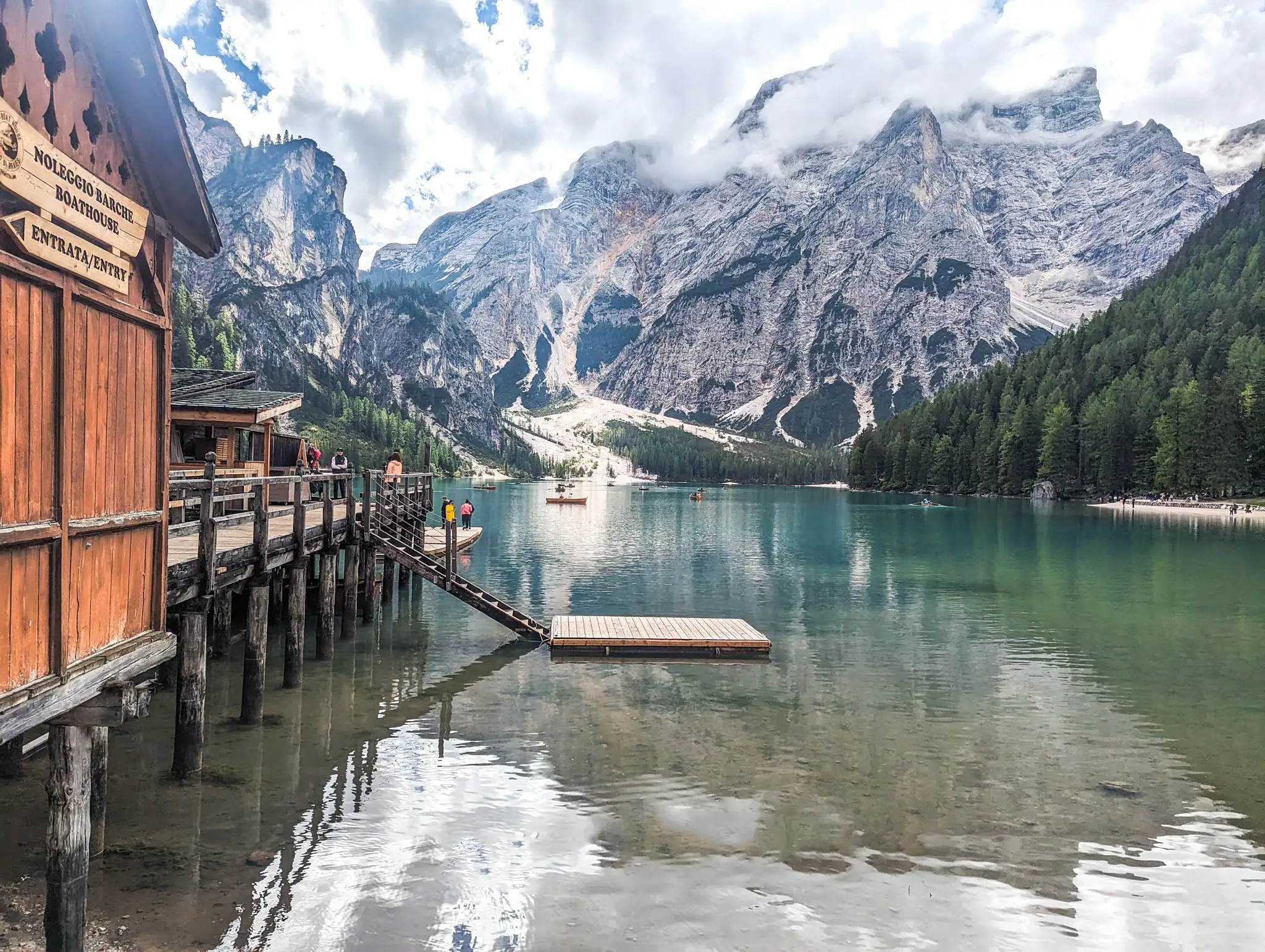People on a floating pontoon floating on a blue lake, rowing boats with mountains in the background
