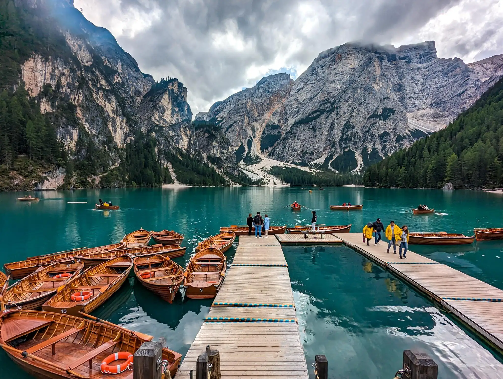 People on a floating pontoon floating on a blue lake, tide down rowing boats with mountains in the background