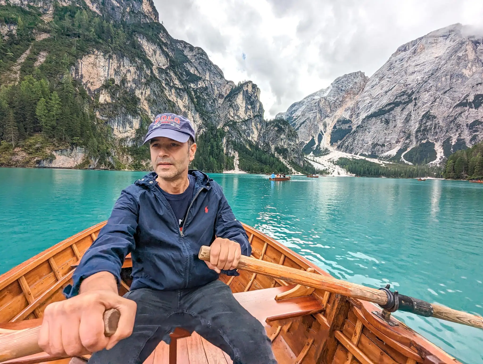 a closeup of a man trying to row the boat, blue lake and mountains