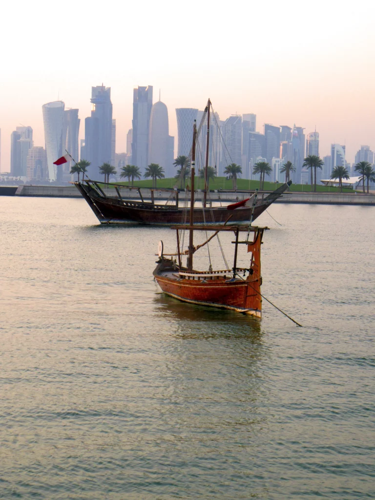 A classical shaped boat at sunset, with the skyscrapers in the far background