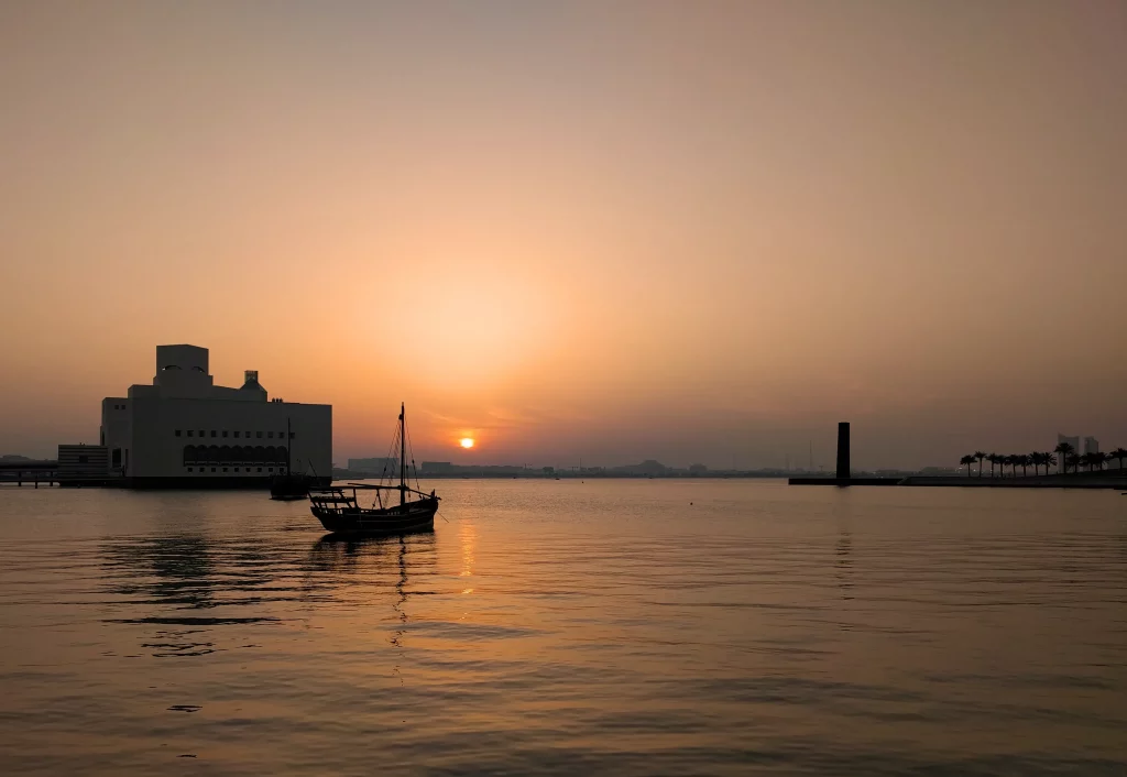 A classical shaped boat at sunset, with the skyscrapers in the far background