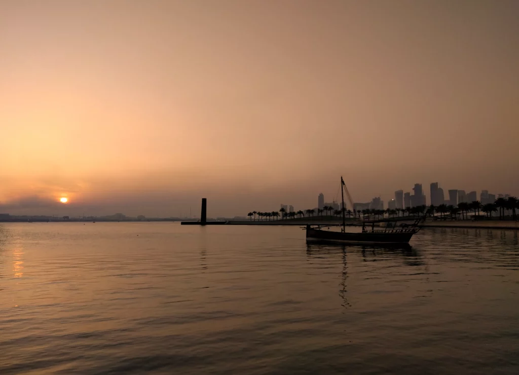 A classical shaped boat at sunset, with the skyscrapers in the far background