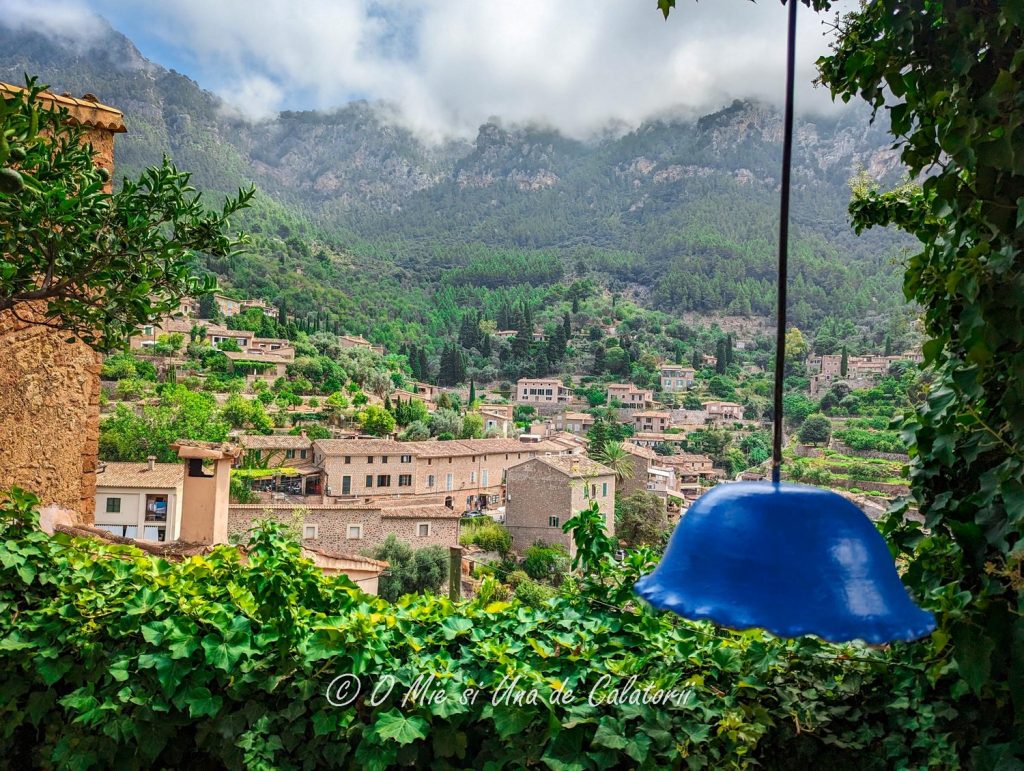 A top view of the village of Deia, with multiple rooftops and greenery all over the place and mountains in the far view