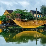 A fish net left to dry over water, with yellow houses in the background