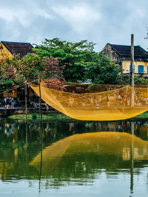 A fish net left to dry over water, with yellow houses in the background