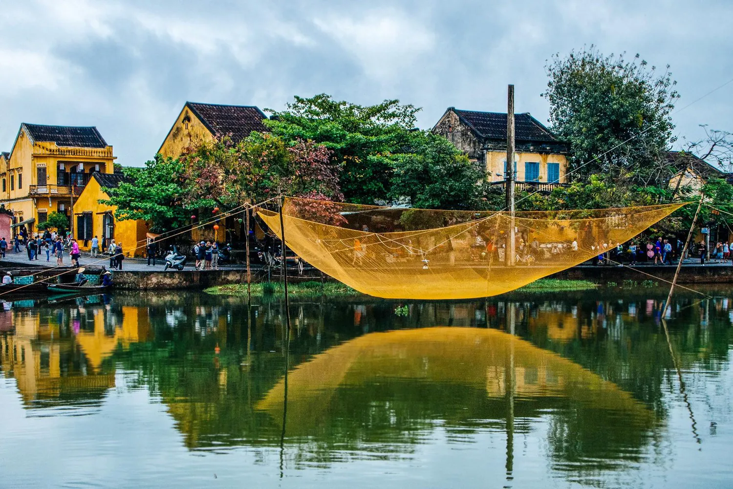 A fish net left to dry over water, with yellow houses in the background