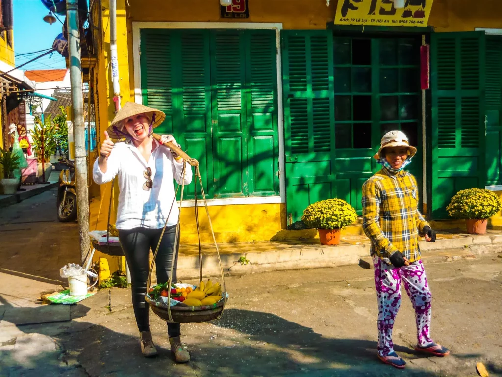 Alina standing for a Photo holding a traditional tool to carry two baskets on a stick full with fresh fruits