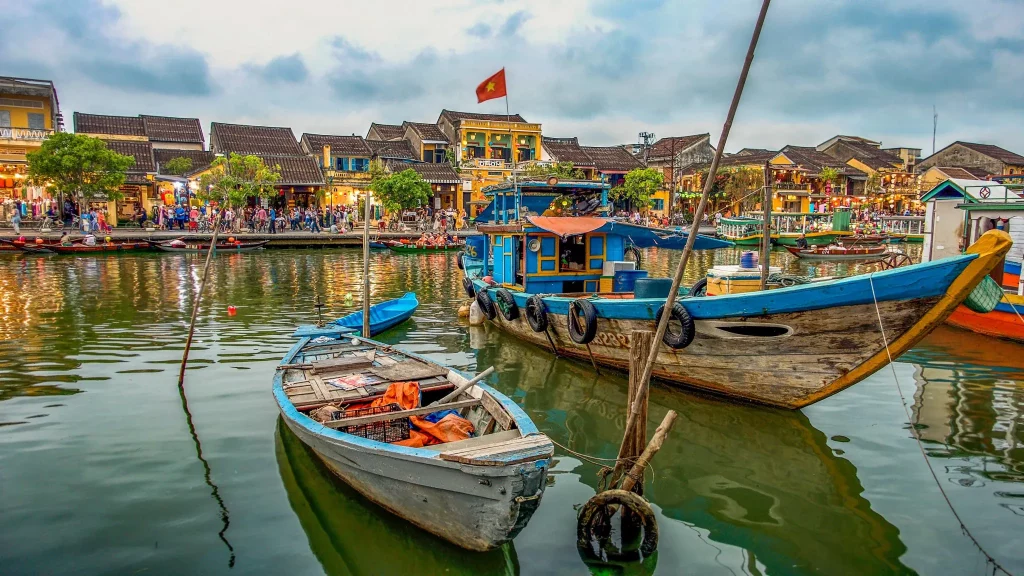 a river with blue fishing boats in the foreground and traditional yellow houses in the background